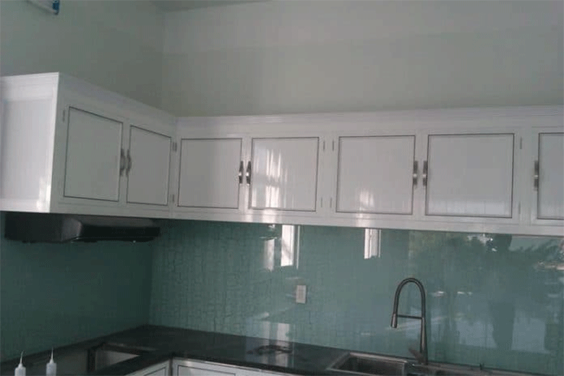 Tủ bếp treo tường gam màu trắng nổi bật trên nền gạch ốp bếp xanh ngọc.