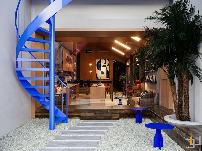 Không gian quán cà phê cổ điển với cầu thang xoắn màu xanh, bàn tròn xanh và cây cọ.